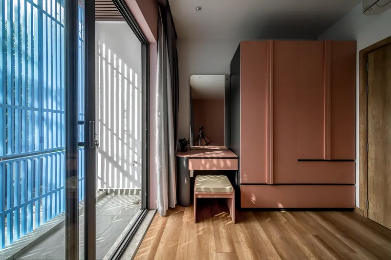 Bedroom with terracotta built-in wardrobe and writing desk beside glass block window casting striped shadows on timber flooring