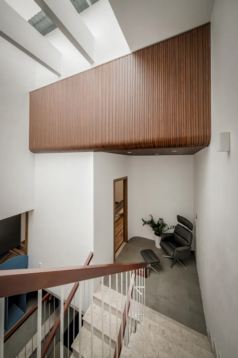 Double-height void with vertical timber-clad volume suspended above a ground floor seating area beneath a skylight
