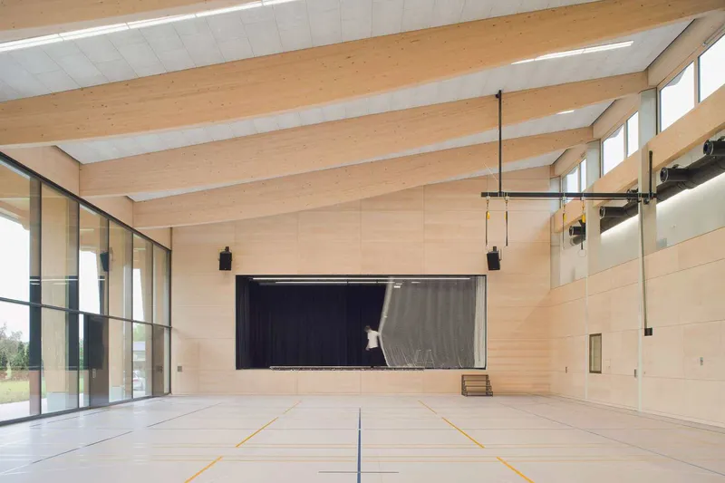 Gymnasium interior with exposed timber beams, clerestory windows and retractable stage curtain