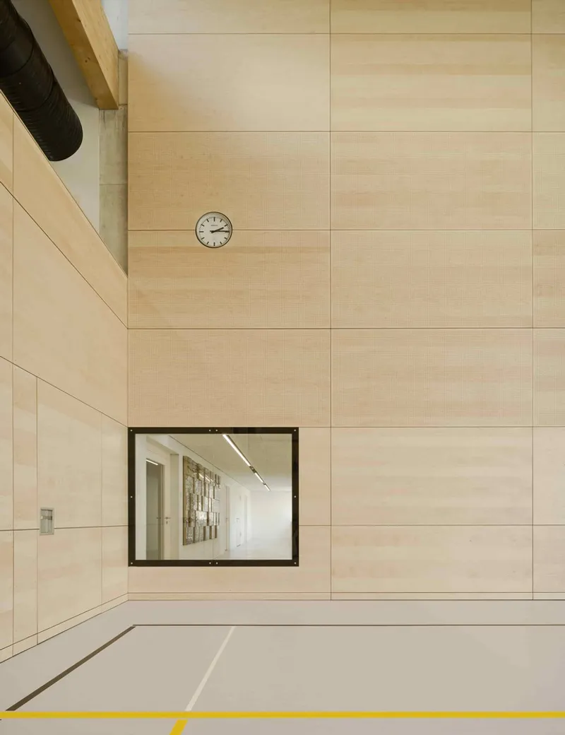 Plywood wall with framed interior window and round clock mounted above a corridor entrance