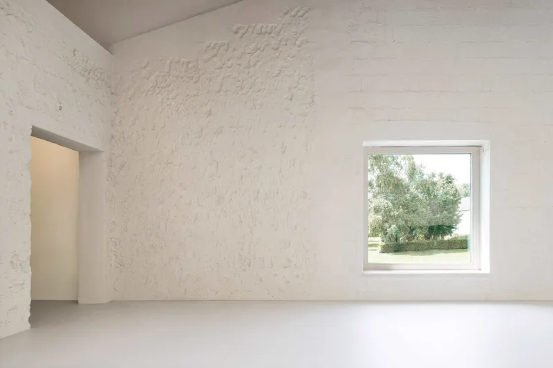White plastered room with textured wall surface and square window framing exterior greenery