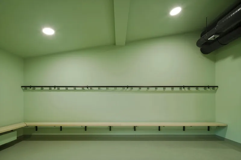 Green changing room with timber bench, wall hooks and exposed ductwork under flush ceiling lights