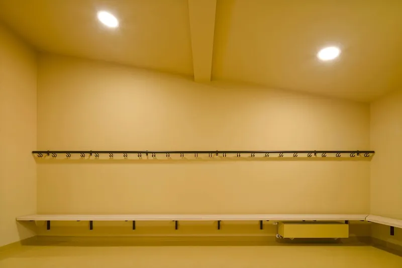 Changing room with continuous bench and coat hooks along yellow plastered walls