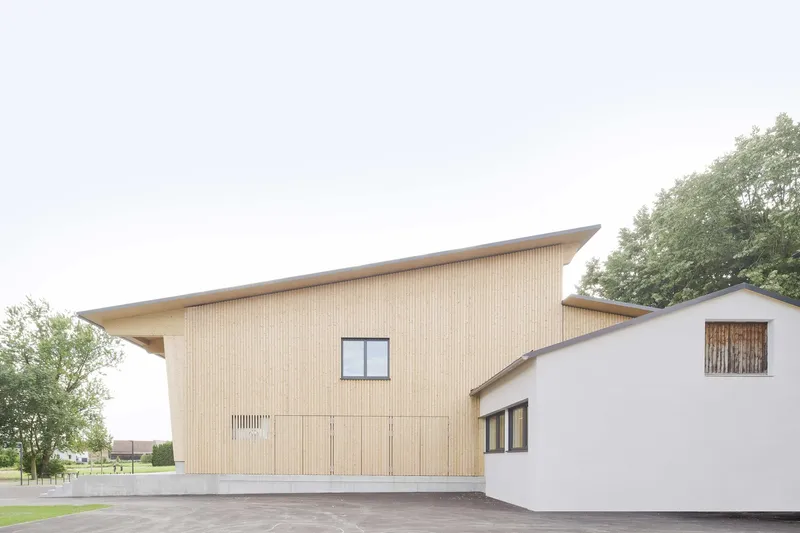 View of the timber-clad volume with sloped roof adjoining the white rendered block under overcast skies
