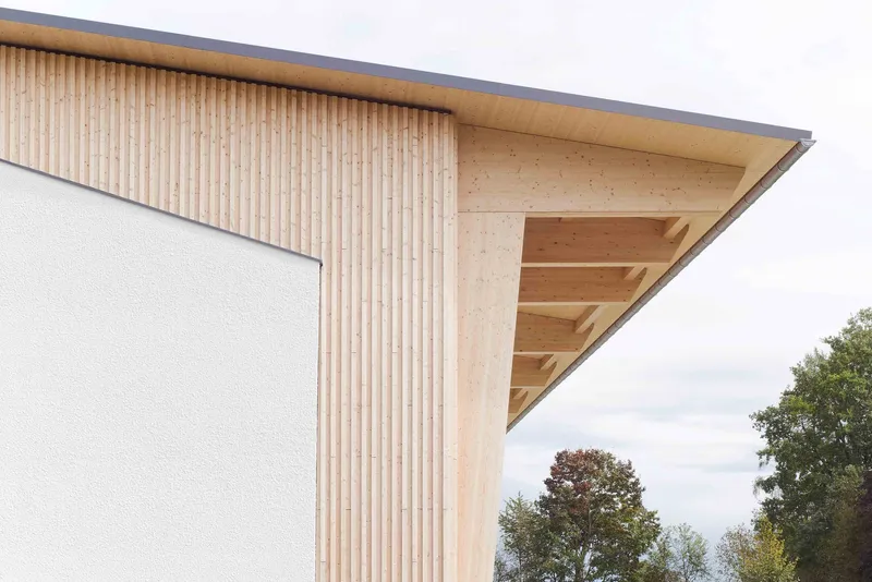 Detail of the vertical timber cladding meeting the exposed soffit beams beneath an overhanging roof edge