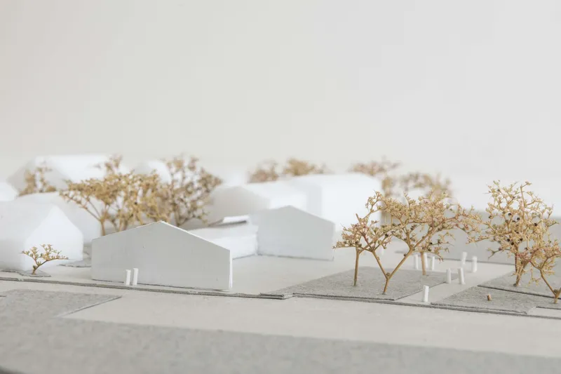 Physical model view showing multiple connected volumes with gabled roofs set among landscape trees