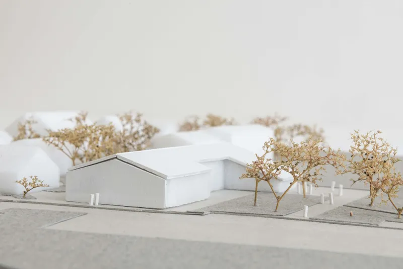 Physical model depicting a double gabled structure with lower connecting wing in a landscaped setting