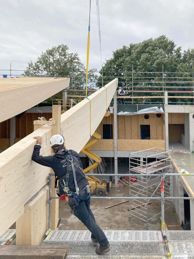 Construction worker guiding a timber roof panel into place using a crane and yellow straps
