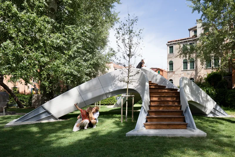 Folded metal canopy with timber stairs in a tree-lined courtyard with children playing