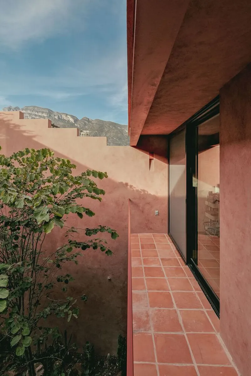Narrow tiled walkway with pink stucco walls and an overhanging soffit under blue sky