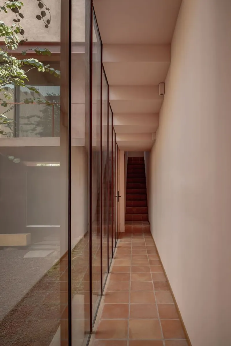 Long corridor with terracotta tile floor and red metal framed glazing along the courtyard