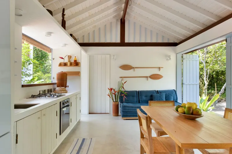 Open living and dining space with vaulted ceiling showing painted timber beams and board paneling