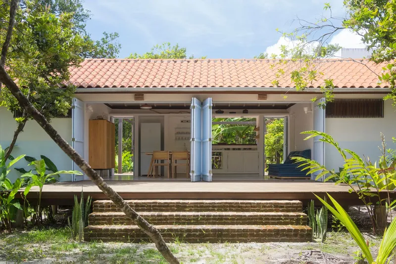 Elevated deck and open-plan interior with terracotta tile roof framed by banana palms and deciduous trees