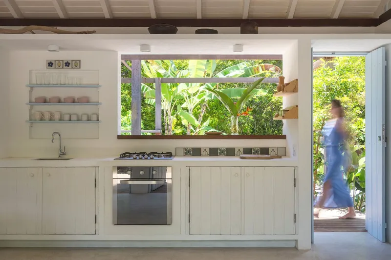 Kitchen counter with horizontal window framing banana palms and a person passing outside