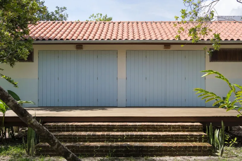 Pale blue vertical wood garage doors beneath a terracotta tile roof with low brick steps and tropical plants