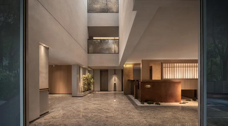 Double-height lobby with textured stone flooring and suspended metal screens at twilight