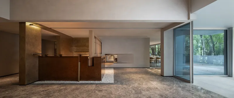 Open plan interior with concrete floors and weathered steel kitchen island under flat concrete beams