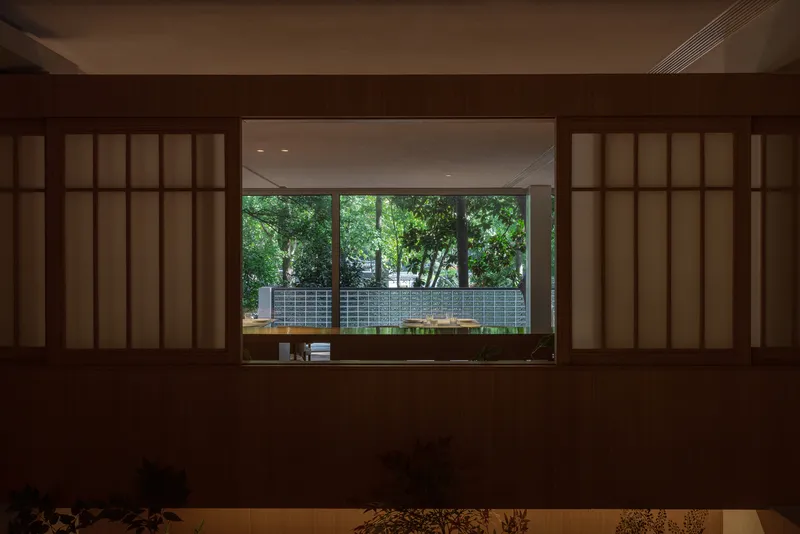 View through timber shoji partition screens toward glazed courtyard with ceramic tile wall beyond