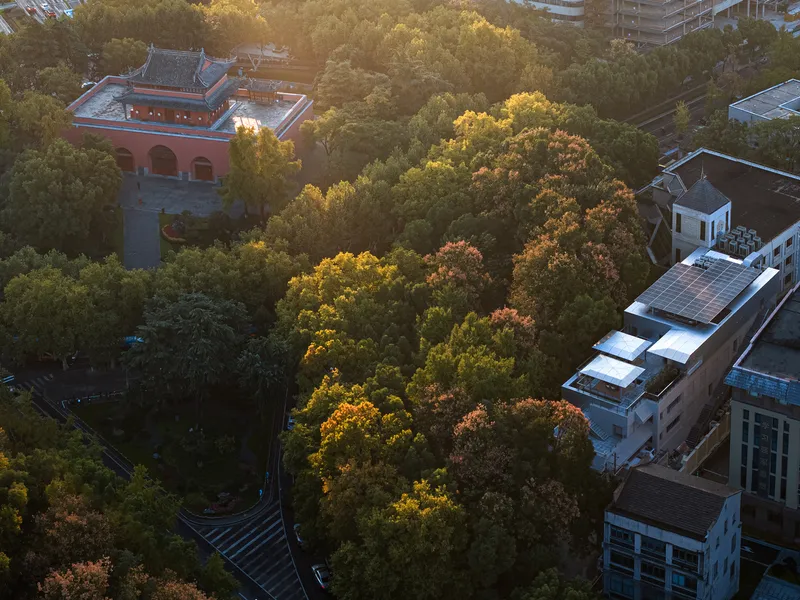 Aerial view of a red-walled pavilion with curved roof nestled among autumn trees at dusk