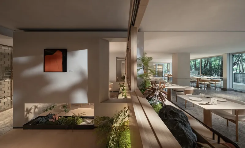 Interior sunken garden with planted beds, rock formations, timber benches, and dappled sunlight filtering across white walls