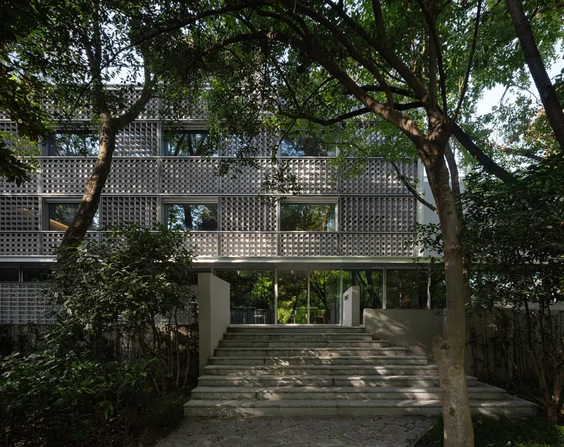 Stone staircase ascending through the wooded site toward the lattice-screened upper floors