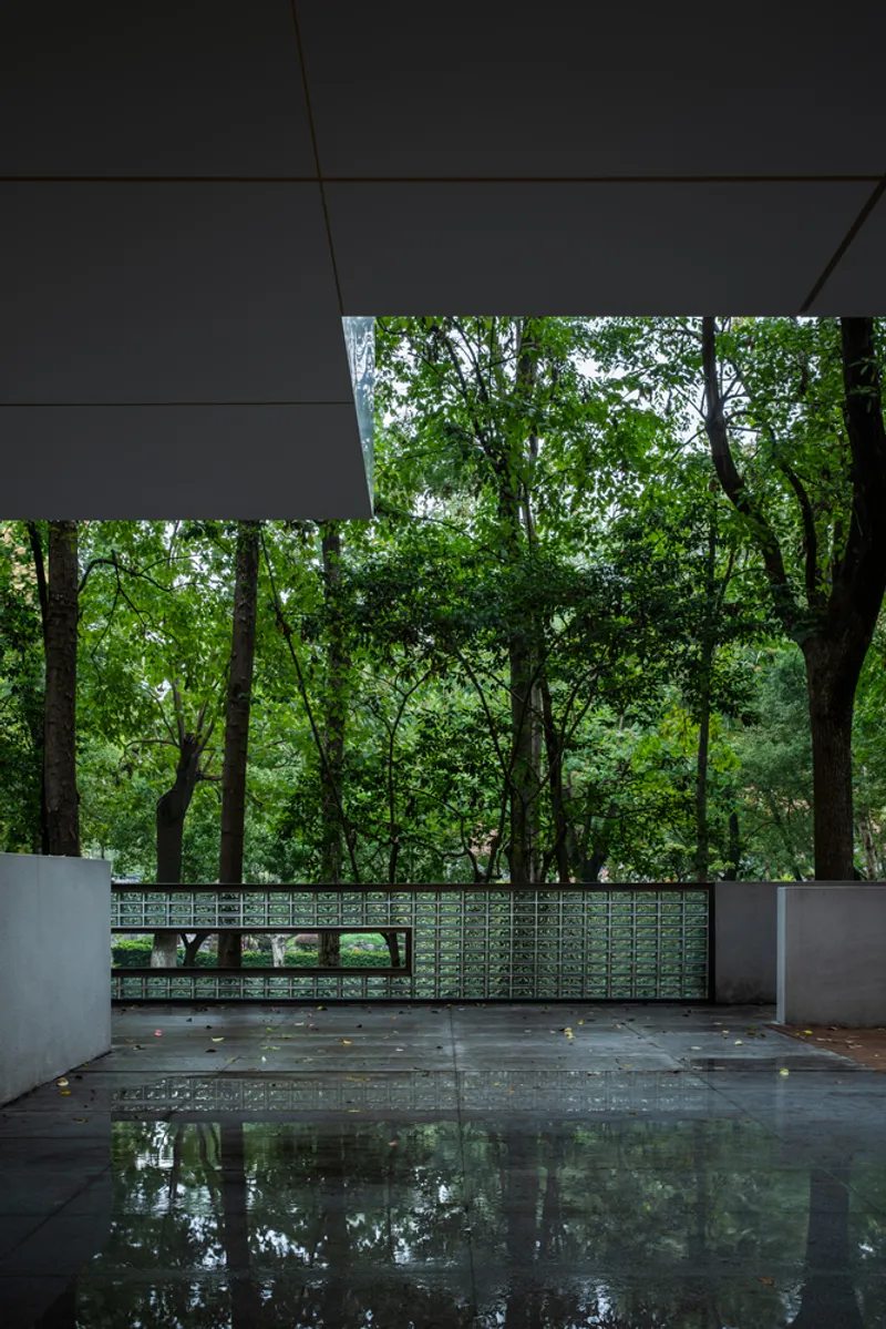 Wet terrace floor reflecting trees beyond a low patterned parapet wall under a cantilevered soffit