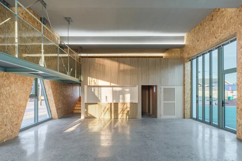 Interior volume with OSB walls, suspended walkway, freestanding timber-clad box, and afternoon sunlight streaming through glazing