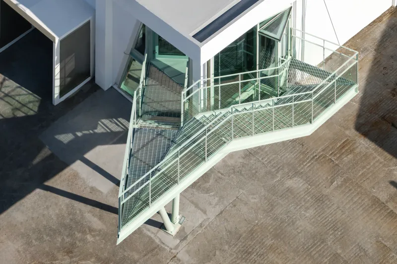Overhead view of green steel staircase with mesh treads casting shadows on polished concrete below