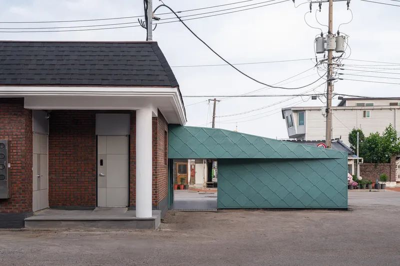 Street view showing dark brick entrance pavilion next to green diamond-patterned metal clad volume under overcast sky