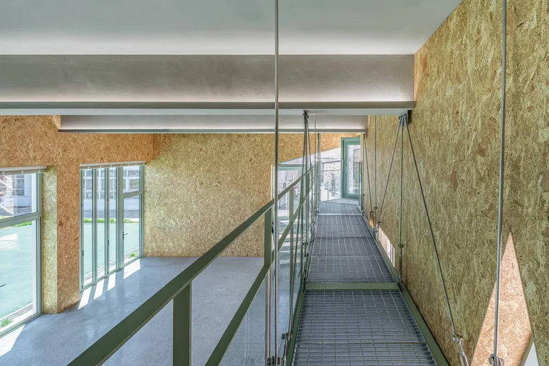 Suspended steel mesh bridge with wire tension cables spanning between OSB panel walls under natural light