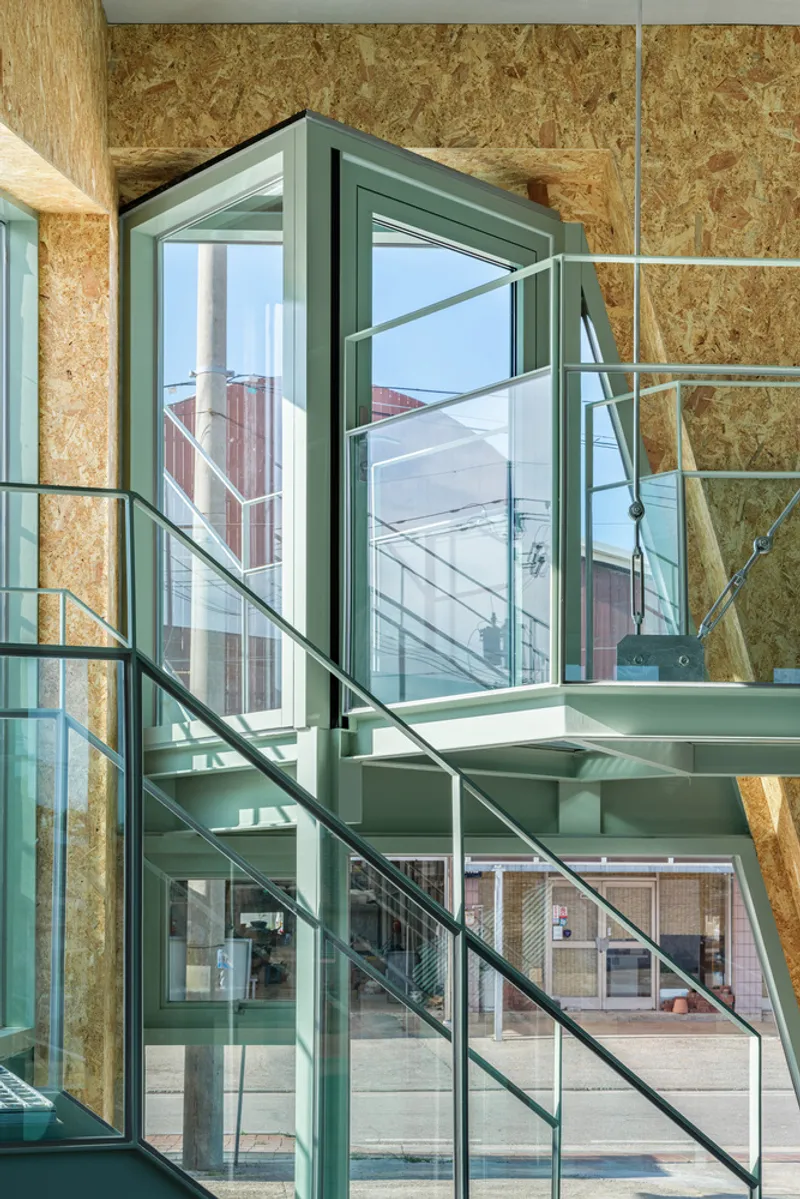 Interior view of a green steel staircase with glass treads framed by oriented strand board walls