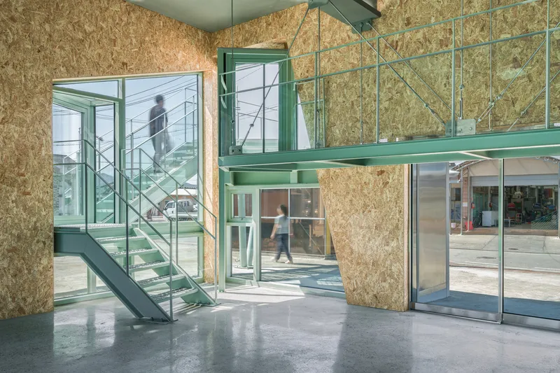 Double-height entrance hall with oriented strand board walls and green steel staircase as figures move through the space