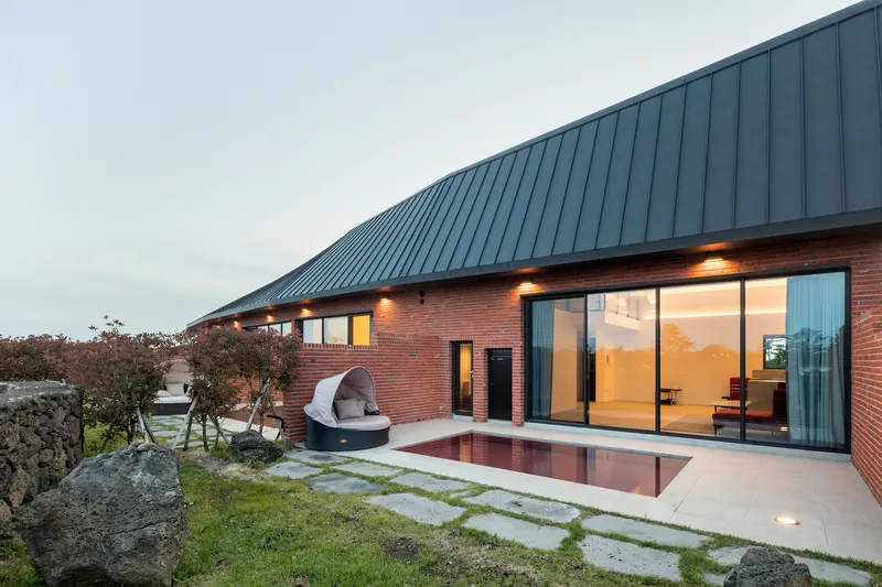 Terrace with stepping stone path and pool at dusk beside full-height glazing and red brick wall