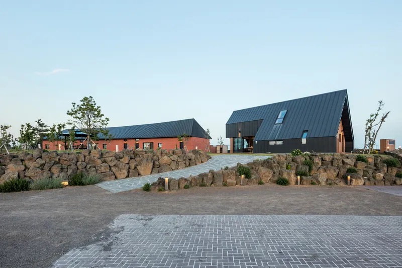 Paved entry plaza with volcanic rock retaining wall leading to clustered gabled volumes