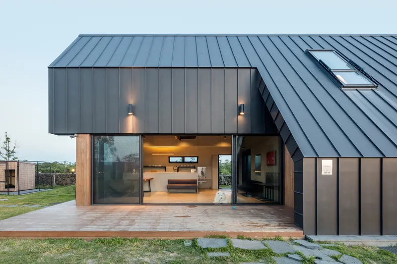Recessed entrance with timber and glass sliding doors beneath a cantilevered metal clad volume