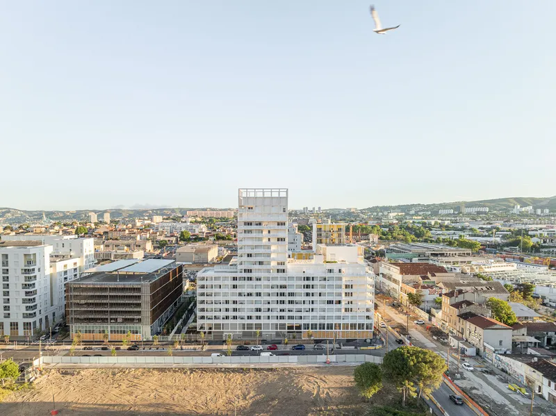 Aerial view of the mixed-use complex with white tower and horizontal blocks in late afternoon light