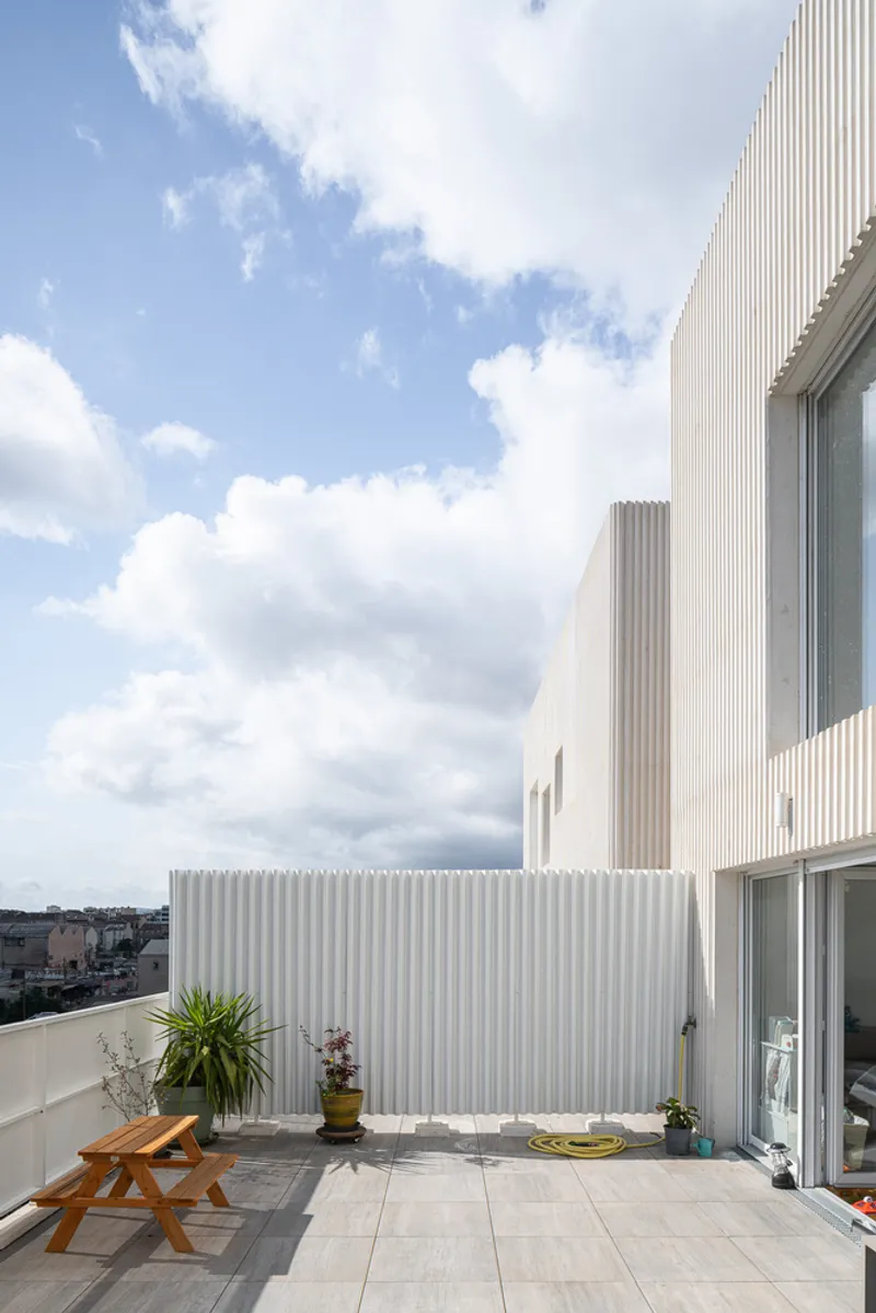 Rooftop terrace with vertical corrugated metal screening and potted plants under scattered clouds