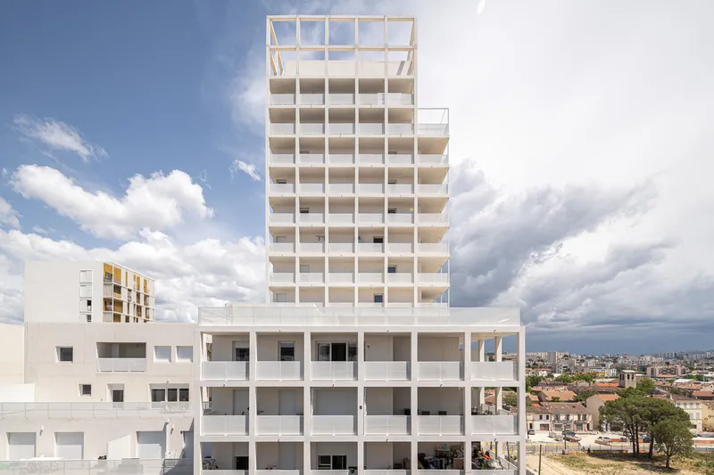 Residential tower rising above a horizontal podium with deep balcony recesses under dramatic clouds