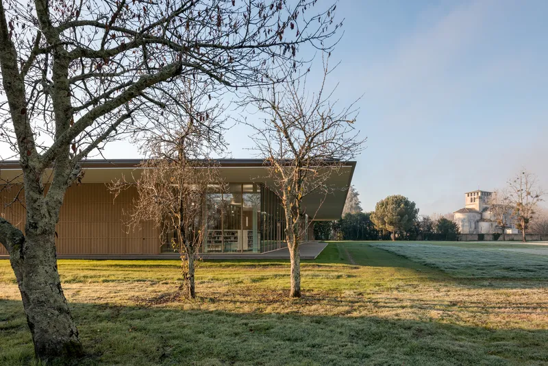 Low timber-clad pavilion set in a frosty lawn with bare winter trees