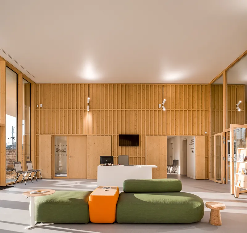 Reception area with vertical wood slat walls and green modular seating under recessed ceiling lights