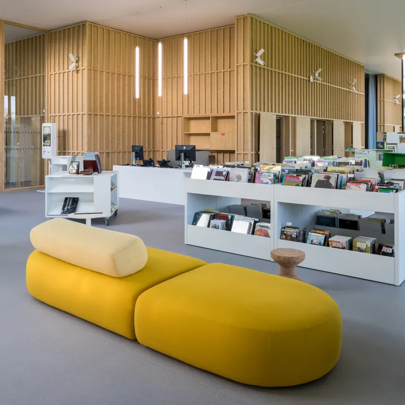 Lending desk with display shelves and yellow upholstered seating in the foreground