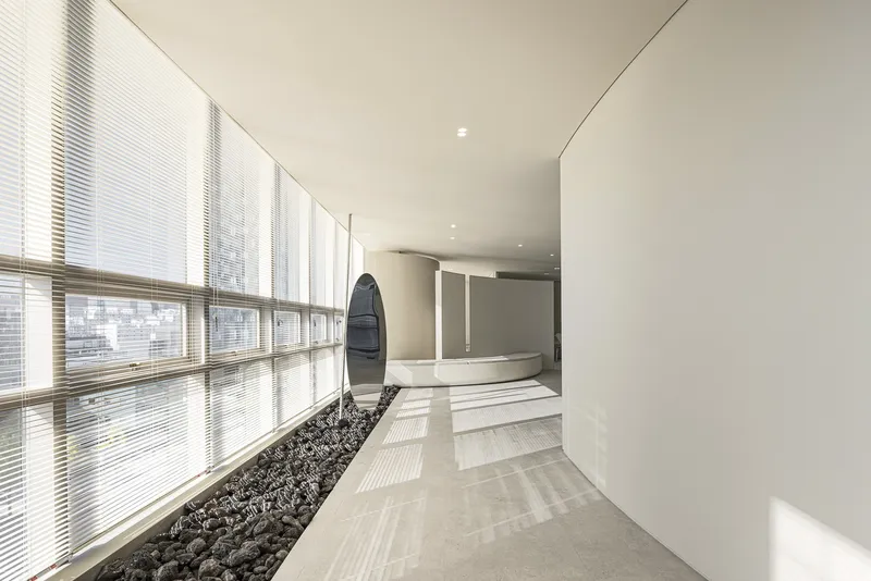 Interior corridor with slatted timber blinds filtering daylight along one wall and dark pebbles in a planted bed