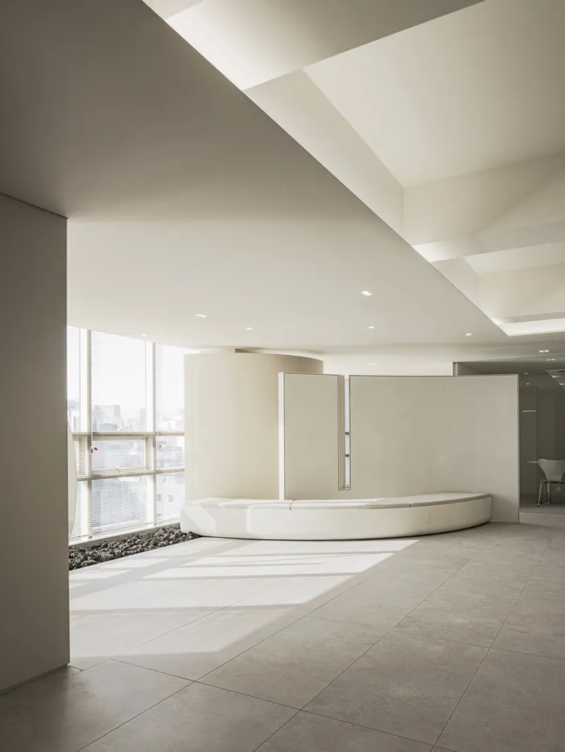 Curved reception desk in a neutral-toned interior with angular skylight above and city views through tall windows