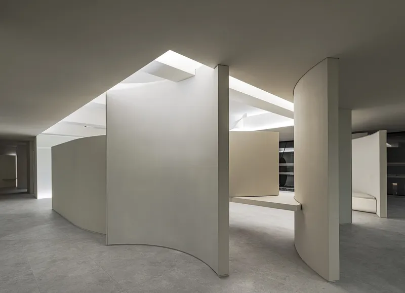 Open office space with curved partition walls and columns beneath geometric skylights casting bright overhead light