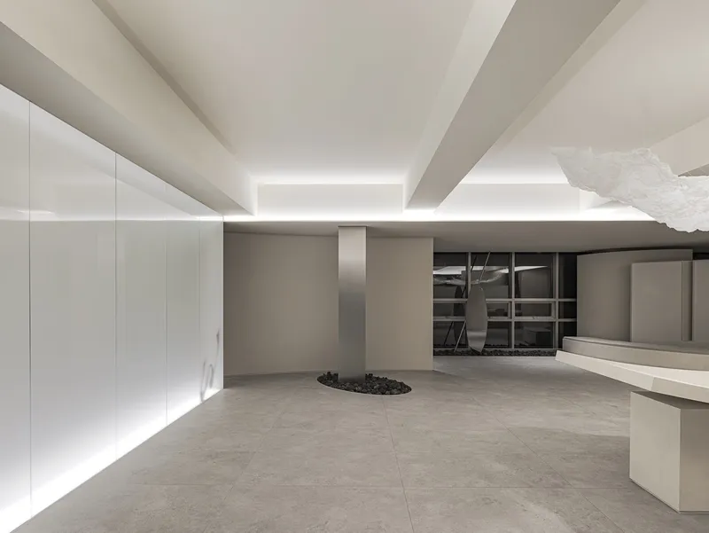 Office interior showing white cabinetry wall, circular planted bed with dark pebbles, and recessed ceiling illumination
