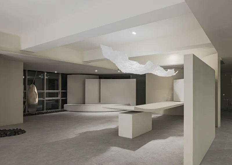 Reception area with floating white sculpture suspended above curved desk and angular partition walls at night