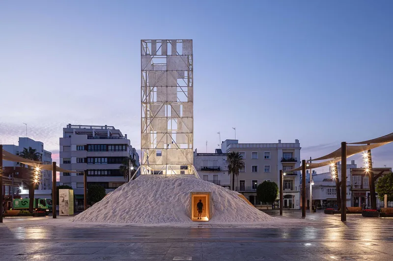 White salt mound with triangular entrance below an illuminated lattice tower at dusk