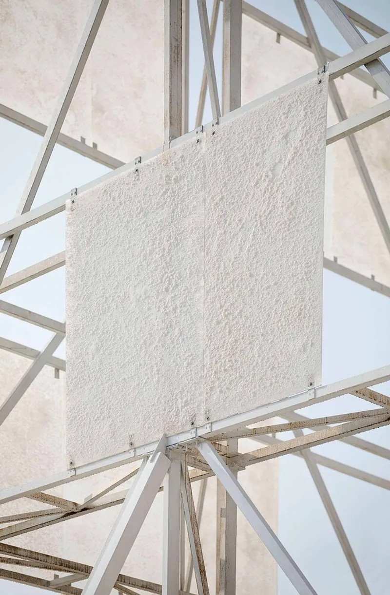 Detail of a textured white panel suspended within the criss-crossing metal bracing