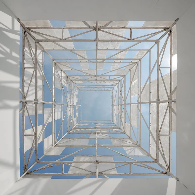 Vertical view up through the steel scaffolding tower framing open sky and concrete panels