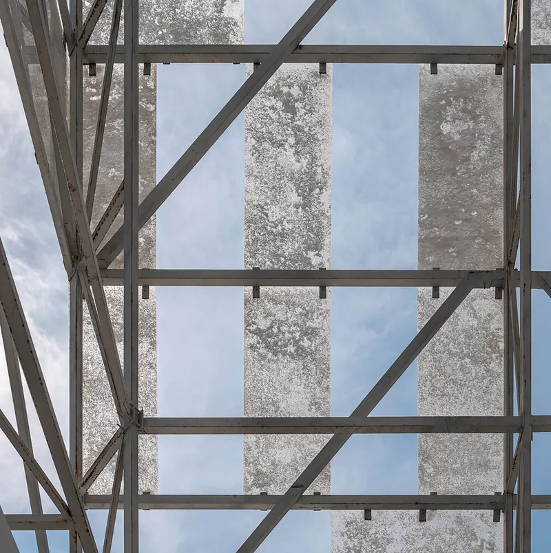 Close-up of weathered concrete panels set within the steel frame grid against cloudy sky